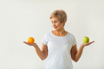 beautiful aged woman with short haircut in a white t-shirt with an apple and an orange on a white background