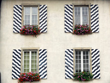 Windows With Striped Decorated Shutters. Ancient Building With Black White Striped Shutters And Red Flower Vases On The Windows