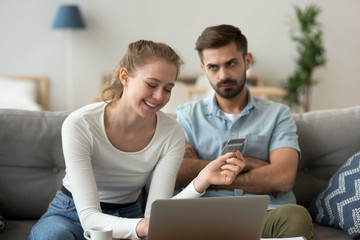 Dissatisfied husband looking at smiling wife shopping online