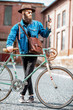 © rh2010 - Portrait of a bearded hipster dressed stylishly with hat and jacket standing with retro bicycle and handgun on the urban background