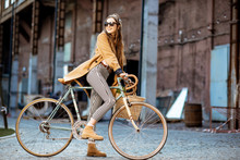 Full Body Portrait Of A Beautiful Stylish Woman Dressed In Coat Standing With Retro Bicycle Outdoors On The Industrial Urban Background