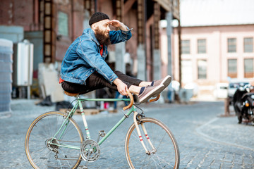 Wall Mural - Stylish man as a crazy hipster having fun, riding retro bicycle outdoors on the industrial urban background