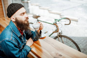 Wall Mural - Stylish man enjoying a coffee drink while sitting at the cafe near the window with retro bicycle outdoors