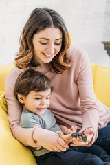 Wall Mural - cheerful mother and son holding funny hamster while sitting on sofa at home