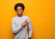 Young african american man over an orange wall smiling and pointing to the side
