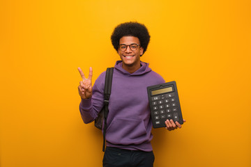 Young african american student man holding a calculator showing number two