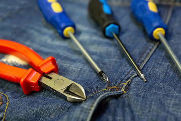 set of screwdrivers focus in center of frame, cross multi-faceted red nippers on jeans close-up