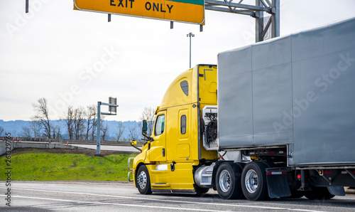 Bright Yellow Big Rig Semi Truck Transporting Goods In Semi Trailer Covered With Black Rubberized Fabric Running On The Wide Highway With Road Signs Buy This Stock Photo And Explore Similar