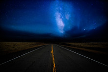 A Highway Disappearing Into The Distance Illuminated By A Star Filled Dramatic Night Sky In A Rural Landscape
