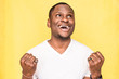 © xartproduction - Portrait of overjoyed man clenches fists with happiness, opens mouth widely, celebrates her success, poses against yellow background.