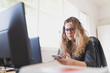 © David Gail/ADDICTIVE STOCK - Concentrated young lady in eyeglasses using mobile phone and sitting at table with monitors in office