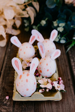 Closeup Set Of Colored Chicken Eggs With Decorative Rabbit Ears In Container On Wooden Background