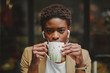 © Miguel Valls/ADDICTIVE STOCK - African American elegant woman with earphones looking at camera, holding mug of beverage and sitting at table in street cafe on blurred background