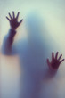 © Nedrofly - Blurred shadow of a horror woman. The hands on the glass. Dangerous person behind frosted glass. Person of mystery Halloween background. Fear, terror, mystery
