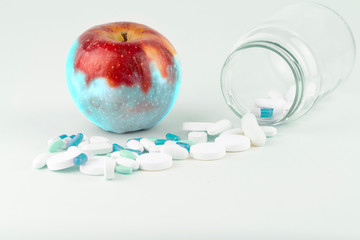 Concept: human GMO manipulation of nature and relative poisoned fruits. Close-up of an apple contaminated by changing color from the medicines in front of it on a white background