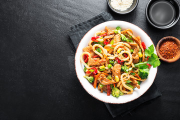 Wall Mural - Udon stir fry noodles with pork meat and vegetables in a white plate on black stone background.