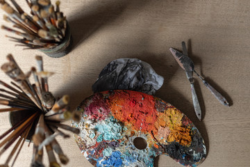 Artist's studio - jar of paint brushes on a wooden table and a colorful palette with paint on