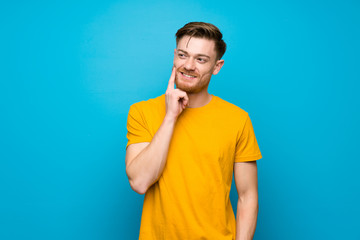 Redhead man over blue wall thinking an idea while looking up