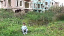 4K Child Sits Alone Near A Deserted Houses On Marshland 