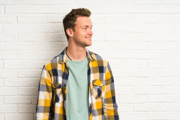 Blonde handsome man over white brick wall standing and looking to the side