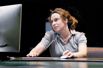 Close-up of an office worker. Woman secretary answering phone calls and talking with customers, she is sitting at her desk working.