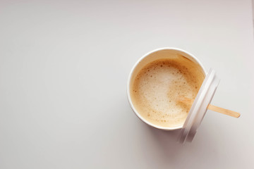 Coffee with a foam in a paper glass on a white background with a plastic lid