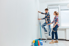 Full-size View Of A Woman Looking While Man Measuring The Wall At New Home. House Renovation DIY Concept.