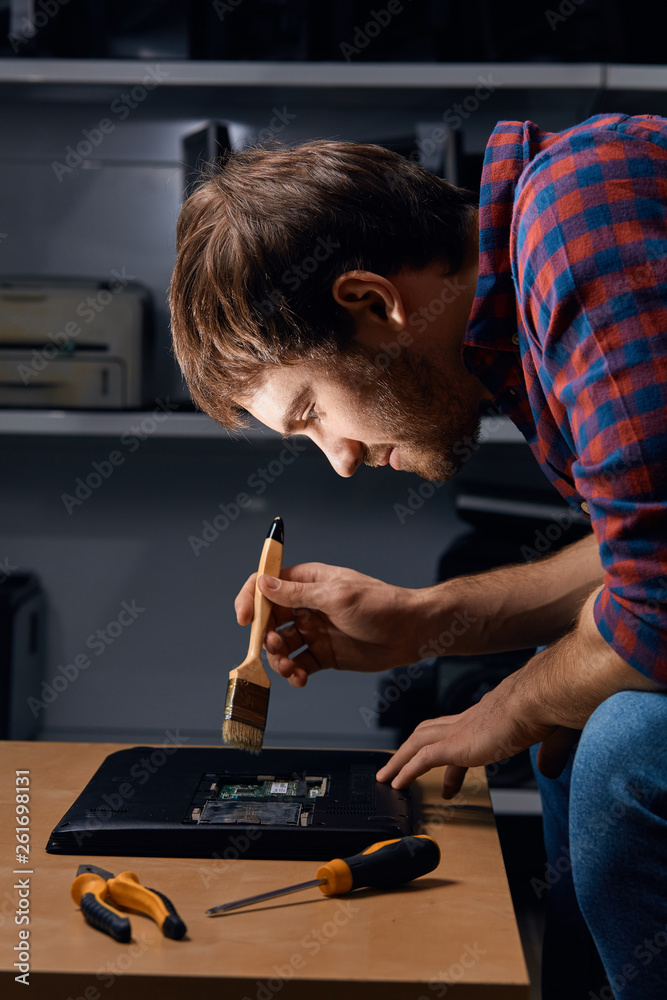 Man Using Brush On Computer handsome man using brush to clean the laptop from the dust, close up ...