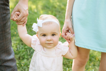 Cute little beautiful girl 6 months walking in the park with parents.