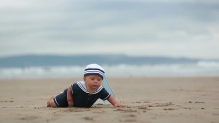 Sticker - Baby boy sitting on the beach near the water and plays with a toy ship and teddy bear