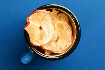 Wall Mural - Apple chips in blue metallic mug in center of bright blue background.