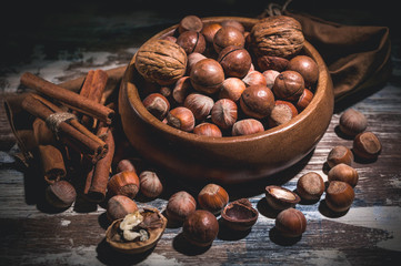 Hazelnut nuts, walnut, cinnamon sticks in a wooden bowl on a dark background. Low key lighting.