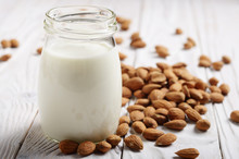 Milk Or Yogurt In Mason Jar On White Wooden Table With Almonds Aside