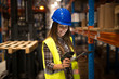 Smiling female worker holding tablet and bar code scanner checking inventory in distribution warehouse. Forklift in background.
