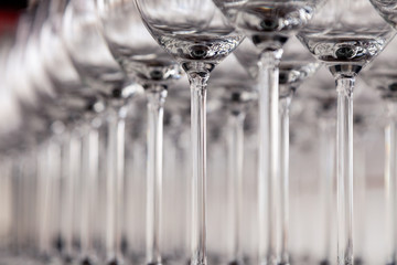 Many transparent crystal wine glasses stand in row on the brown wooden shelves of the rack. Side view. Concept of tasting, banquet, catering, buffet, lunch, anniversary, wedding, birthday