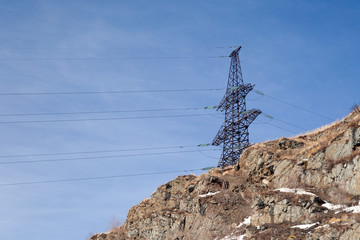 High voltage post transmission power line, electricity distribution station on the mountain with stones on th background of blue sky