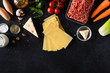 Raw lasagna ingredients and products for pasta background with copy space. Top view and flat lay backdrop of vegetables and herbs on a black concrete stone background