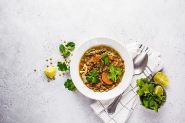 Lentil soup with vegetables in a white plate, white background, top view. Plant based food, clean eating.