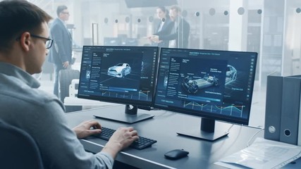 Fototapete - Professional Engineer Works on a Computer with a 3D CAD Software and Tests the Electric Car Chassis Prototype with Wheels, Batteries and Engine Standing in a High Tech Development Laboratory.