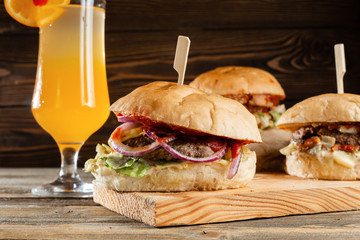 Three big burger with meat cooked on BBQ coal. Lunch with Glass of juice on a wooden background. The concept of fast food and unhealthy food