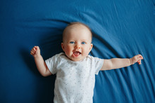 Portrait Of Cute Adorable Smiling White Caucasian Baby Girl Boy With Blue Eyes Four Months Old Lying On Bed In Bedroom Looking At Camera. View From Top Above. Happy Childhood Lifestyle.