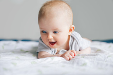 closeup portrait of adorable funny white caucasian baby with blue eyes lying on tummy belly on bed. 