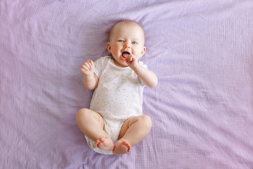 Portrait of cute adorable smiling laughing white Caucasian baby girl boy with blue eyes four months old lying on bed looking at camera. View from top above. Happy childhood lifestyle.