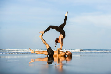 young attractive and beautiful acrobat couple practicing acroyoga exercise concentrated keeping balance practiing yoga on the beach in relaxation and meditation concept