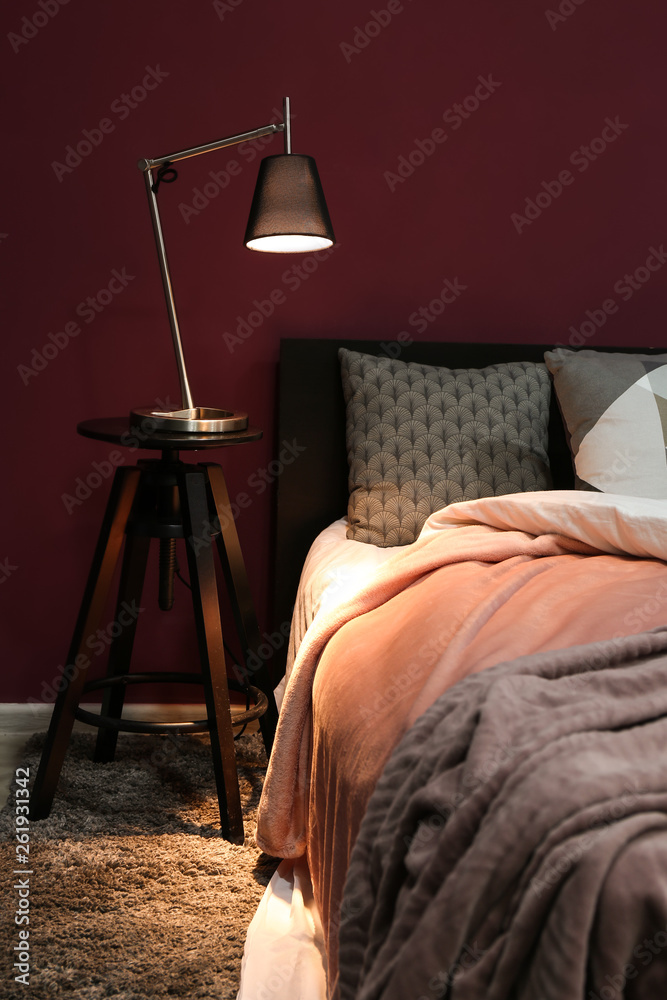 Big comfortable bed with lamp on table in room