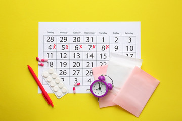 Wall Mural - Menstrual calendar with pads, pills and alarm clock on color background