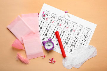 Wall Mural - Menstrual calendar with feminine products and alarm clock on color background