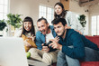 © Alex from the Rock - Group of four friends playing video games at home together using controller in big bright apartment