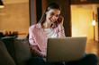 © JustLife - Girl online, using earphones. Teen at home, group chatting on her laptop. Student studying online at home.