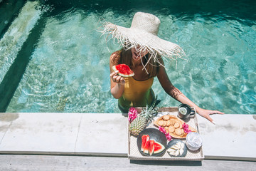 Wall Mural - Girl eating fruits in pool on luxury villa in Bali